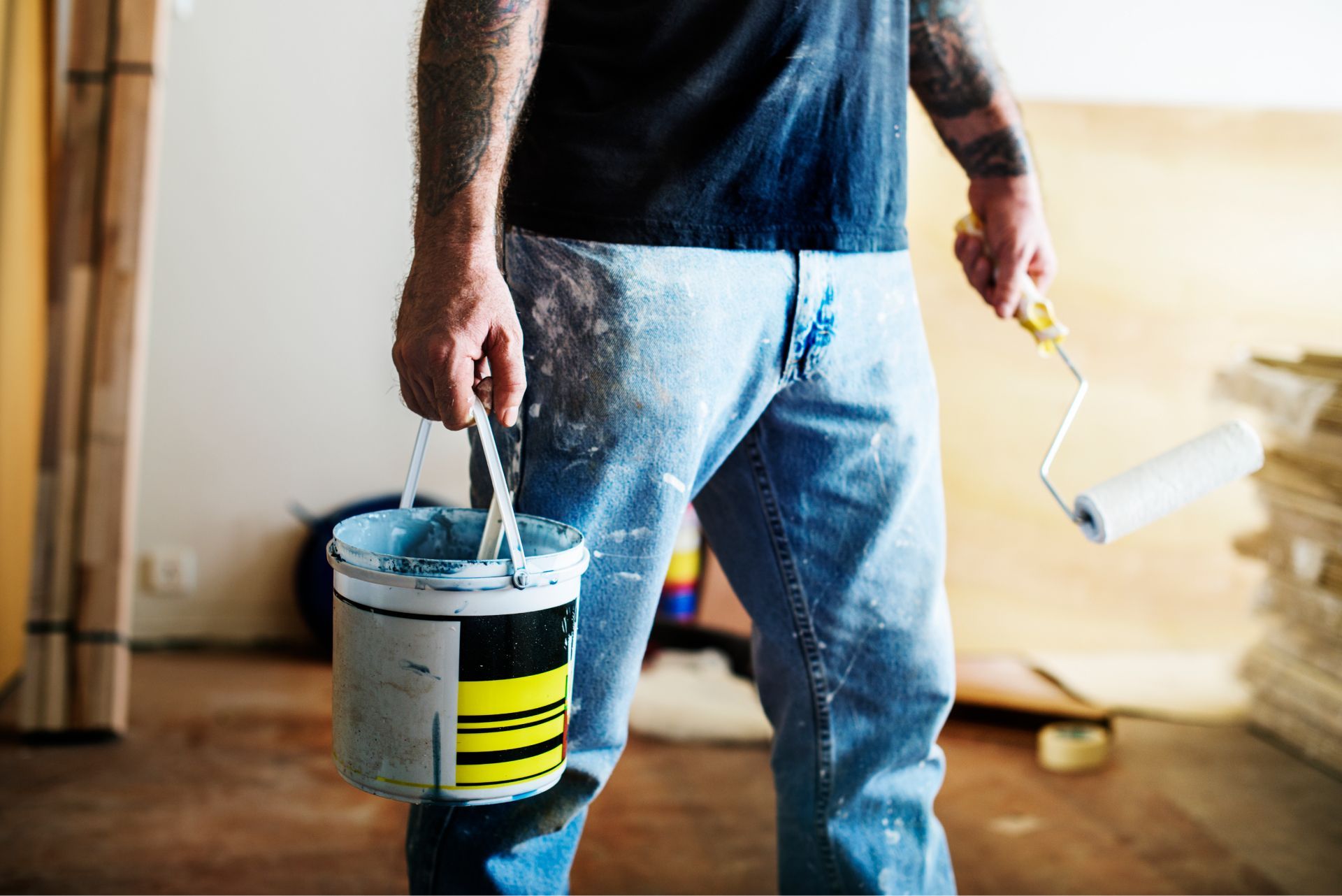 A man is holding a bucket of paint and a paint roller.