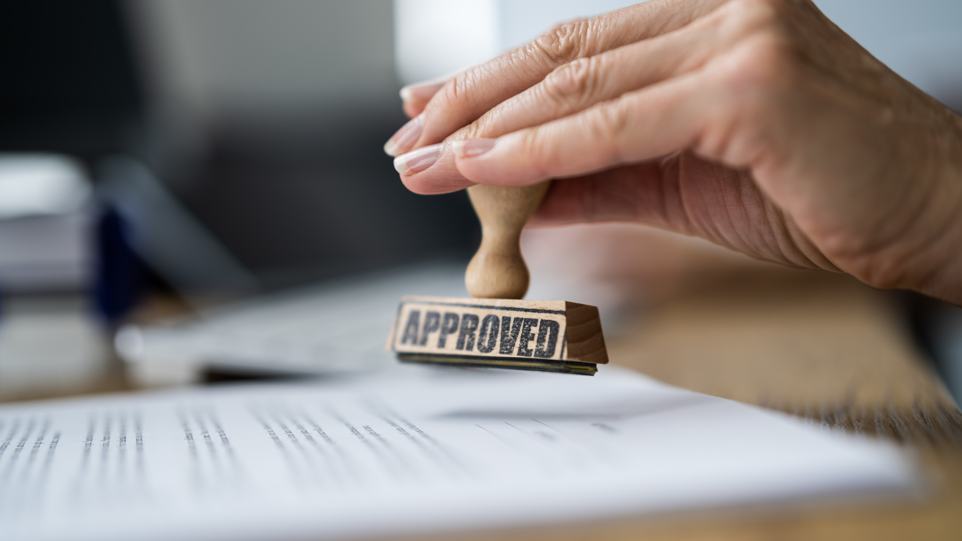 A person is holding a stamp that says approved on a piece of paper.