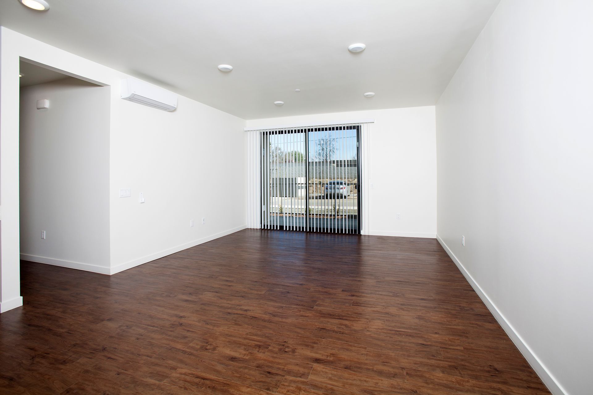 An empty living room with hardwood floors and sliding glass doors.