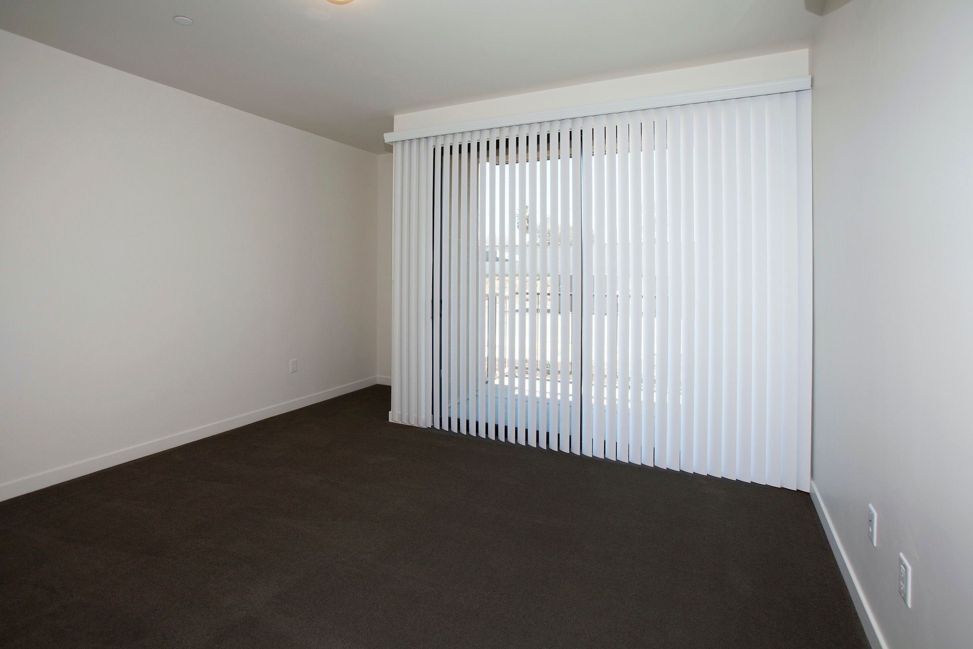 An empty room with a sliding glass door and vertical blinds