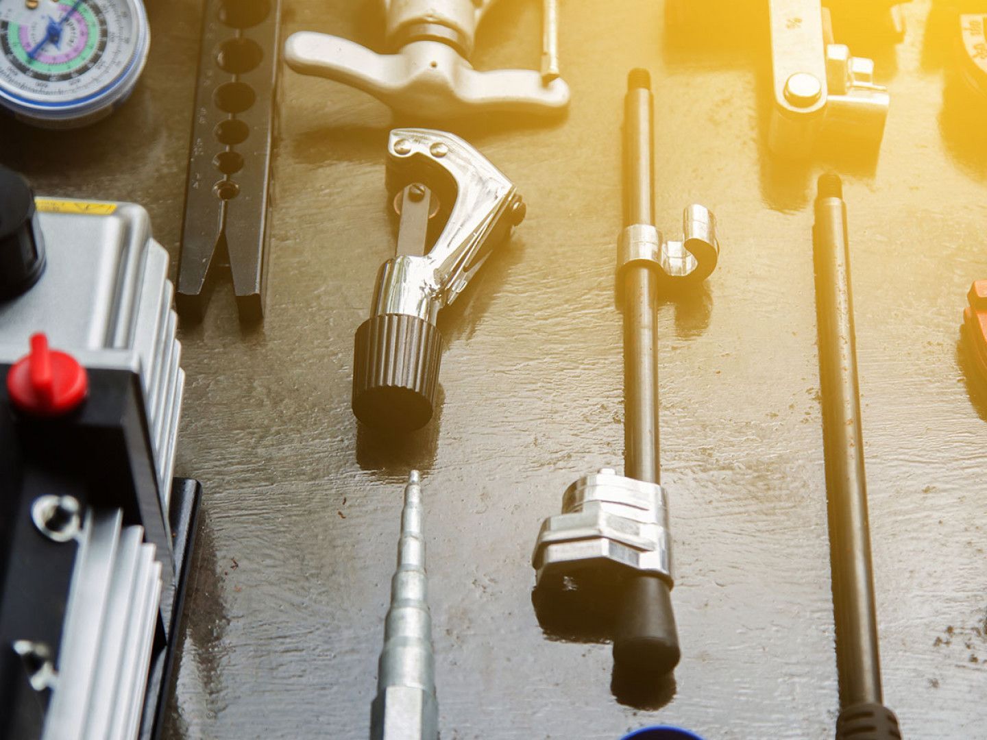 HVAC tools: gauge, tube cutter, flaring tool, vacuum pump, and other tools on a workbench.