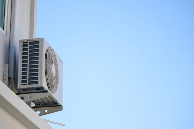 Air conditioner unit mounted on a white building wall against a clear blue sky.