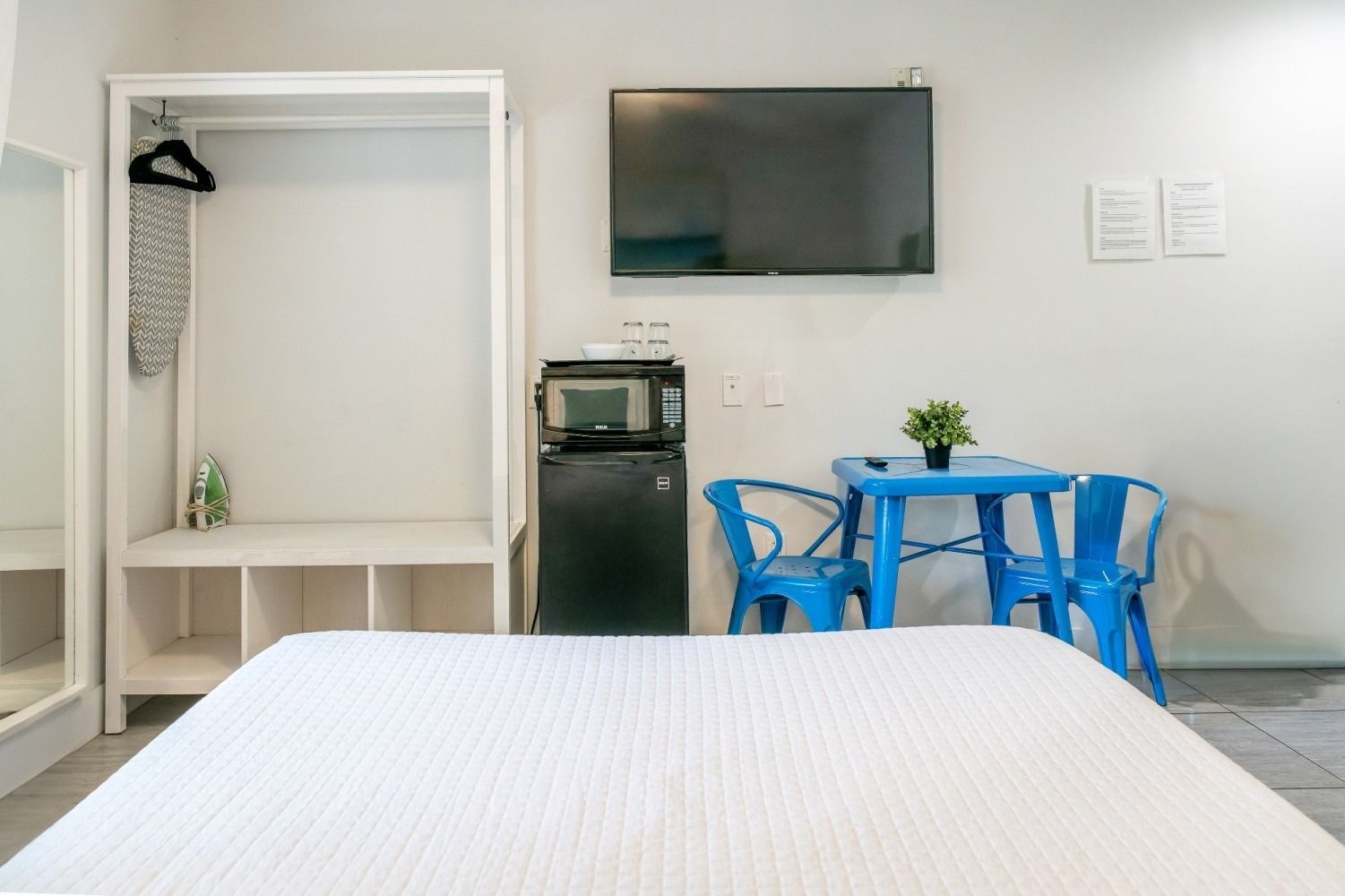 A small studio apartment with a bed, TV, wardrobe, and a blue table and chairs.