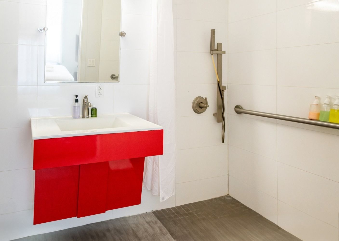 Red vanity in accessible bathroom; white tile, grab bar, shower, and sink.