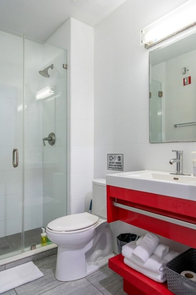 Bathroom with a glass shower, red vanity, and white toilet.