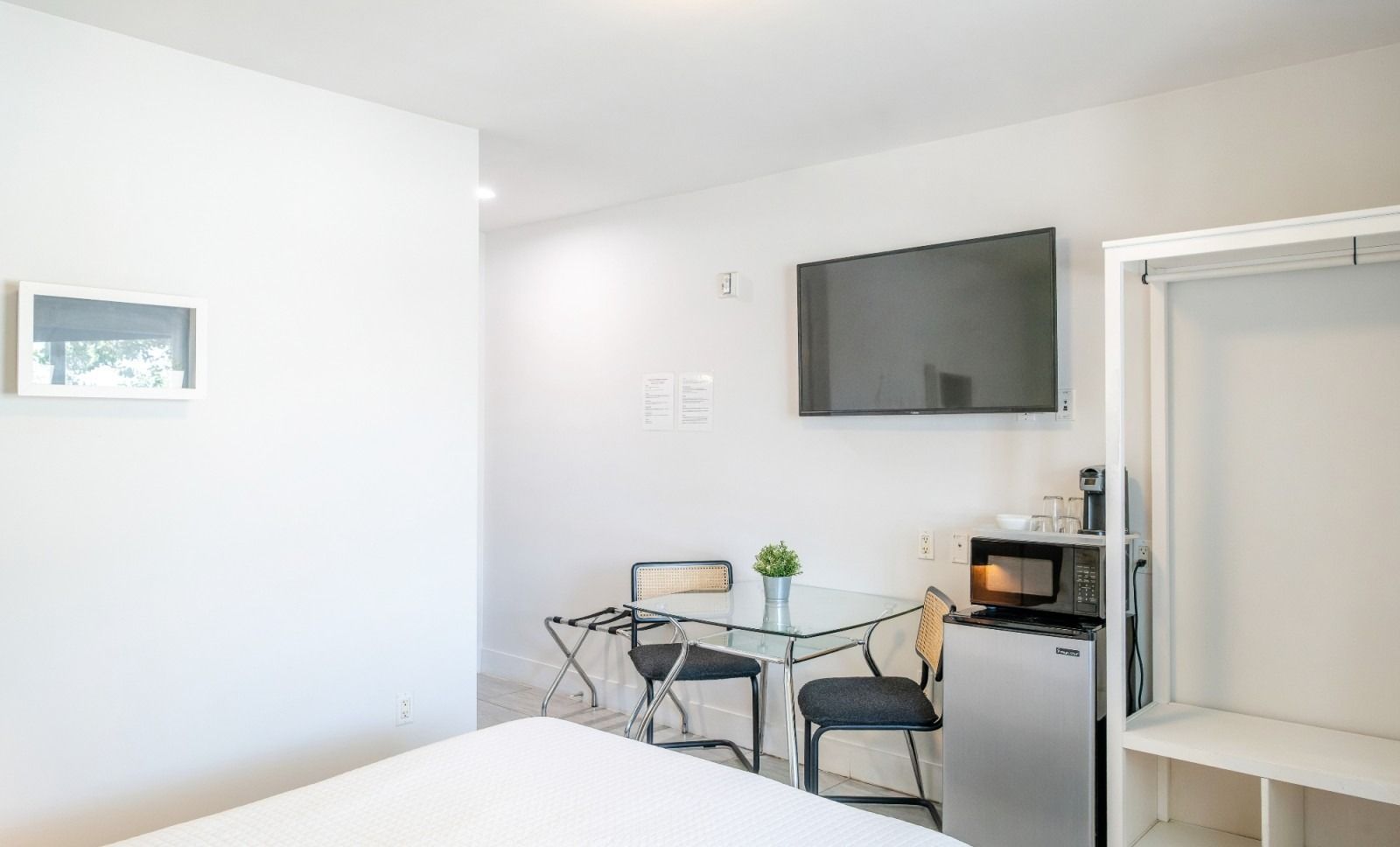 Small hotel room with bed, table, chairs, TV, microwave, and open closet.