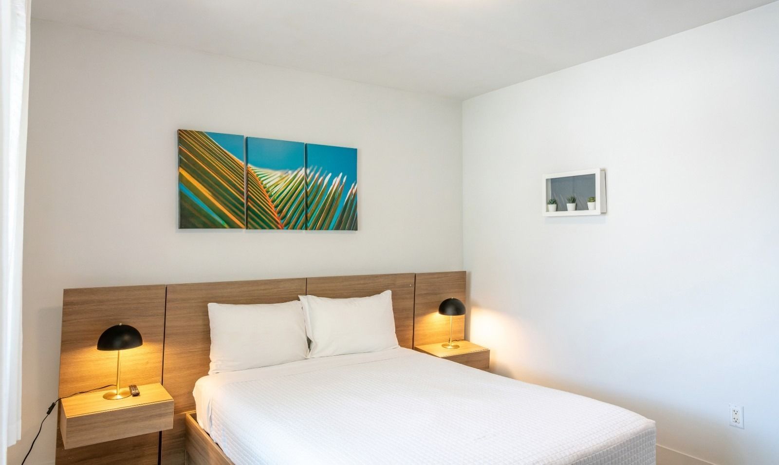 Bedroom with a bed, two nightstands, artwork, and an air conditioning unit. White walls and bedding.