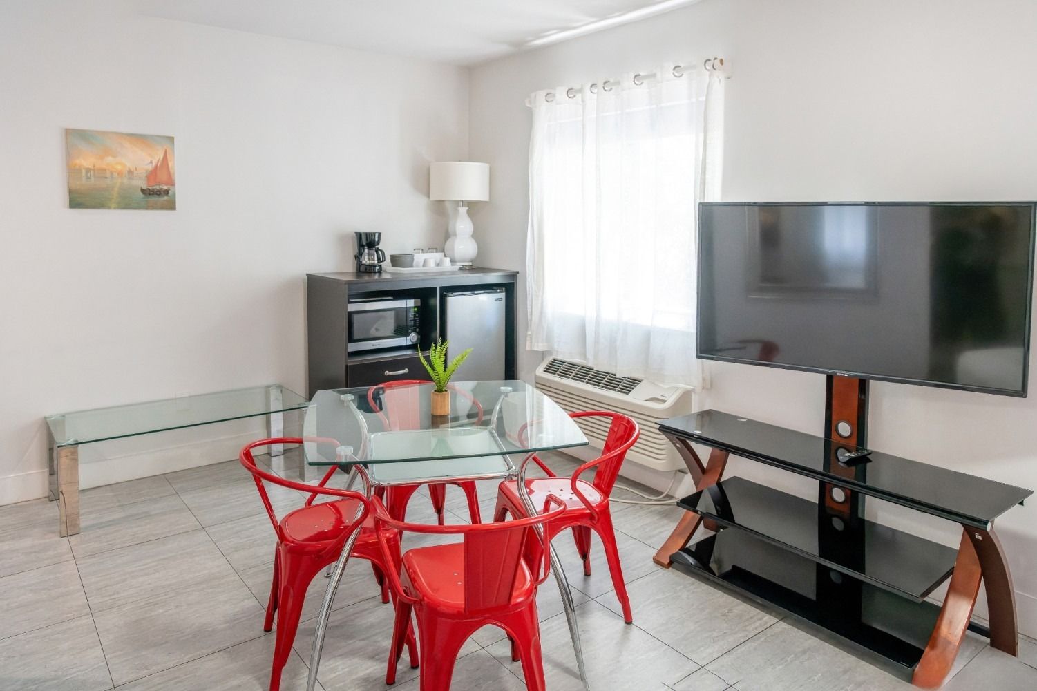 Interior of a room with a dining table, red chairs, a TV, and a mini-fridge.