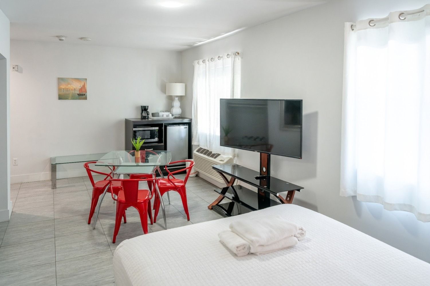 A studio apartment with a bed, TV, table, chairs, microwave, mini-fridge, and a window.