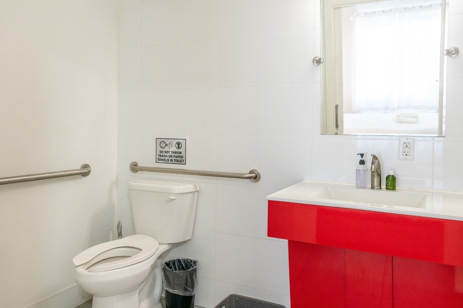A wheelchair-accessible bathroom with a white toilet, red vanity, and grab bars.