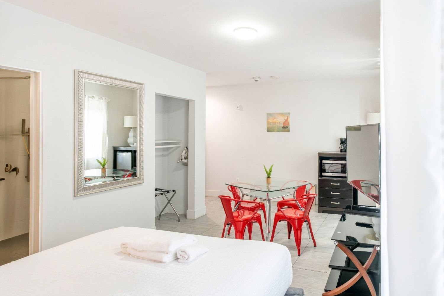 A bright, small studio apartment with a bed, table with chairs, and kitchenette.