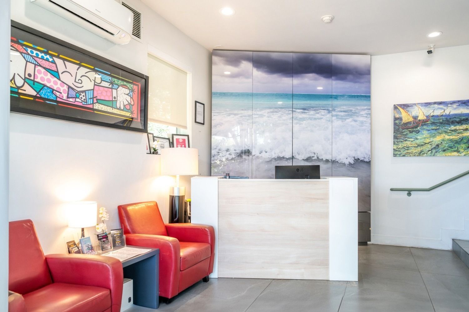 Reception area with red armchairs, art, and a beach scene backdrop.