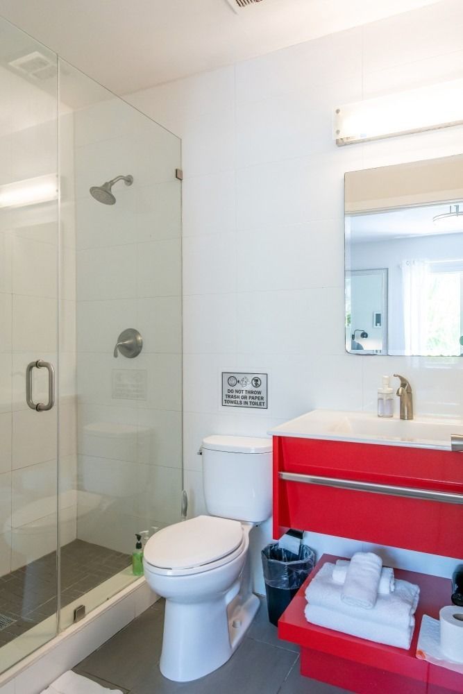 Bright bathroom with red vanity, glass shower, and white fixtures.