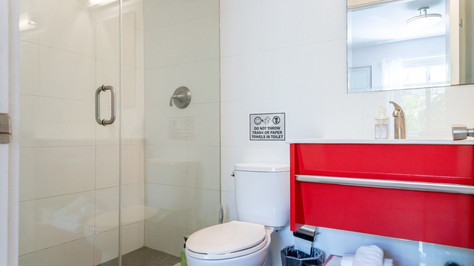 Bathroom with a red vanity, glass shower, white walls, and a toilet.