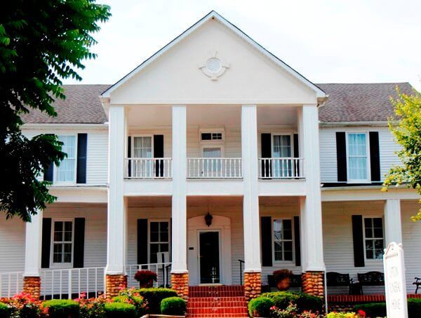 White two-story house with columns and shutters, a red brick porch, and landscaping.