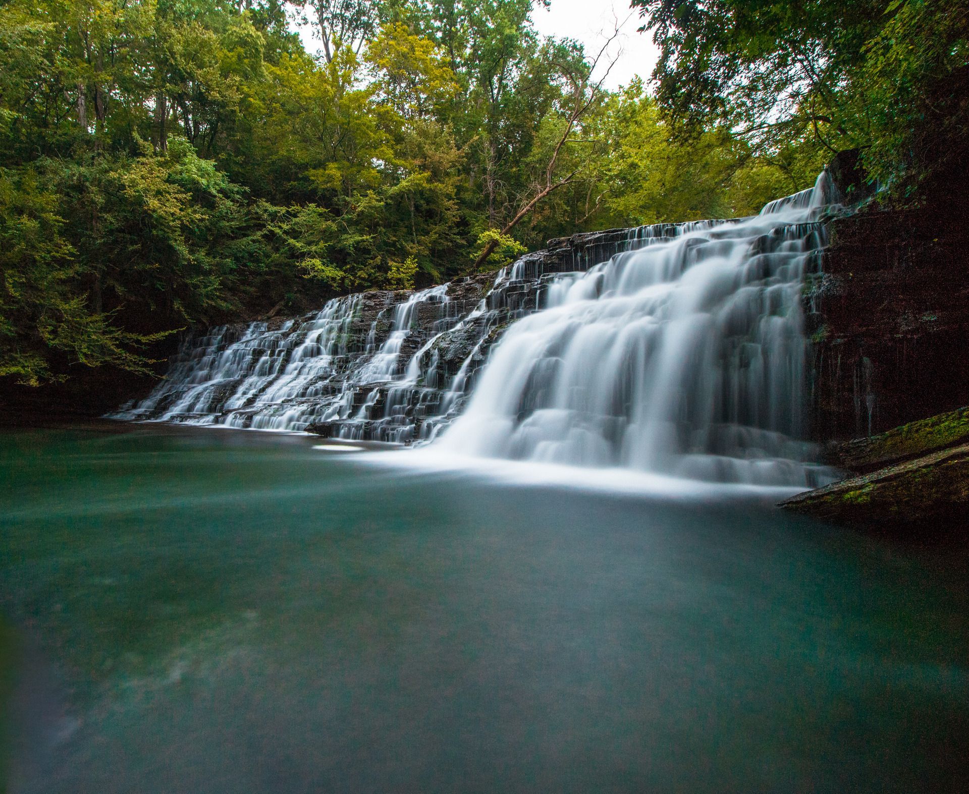 Mature couple looking at laptop in living room; man leans towards woman, sunlight streams in.