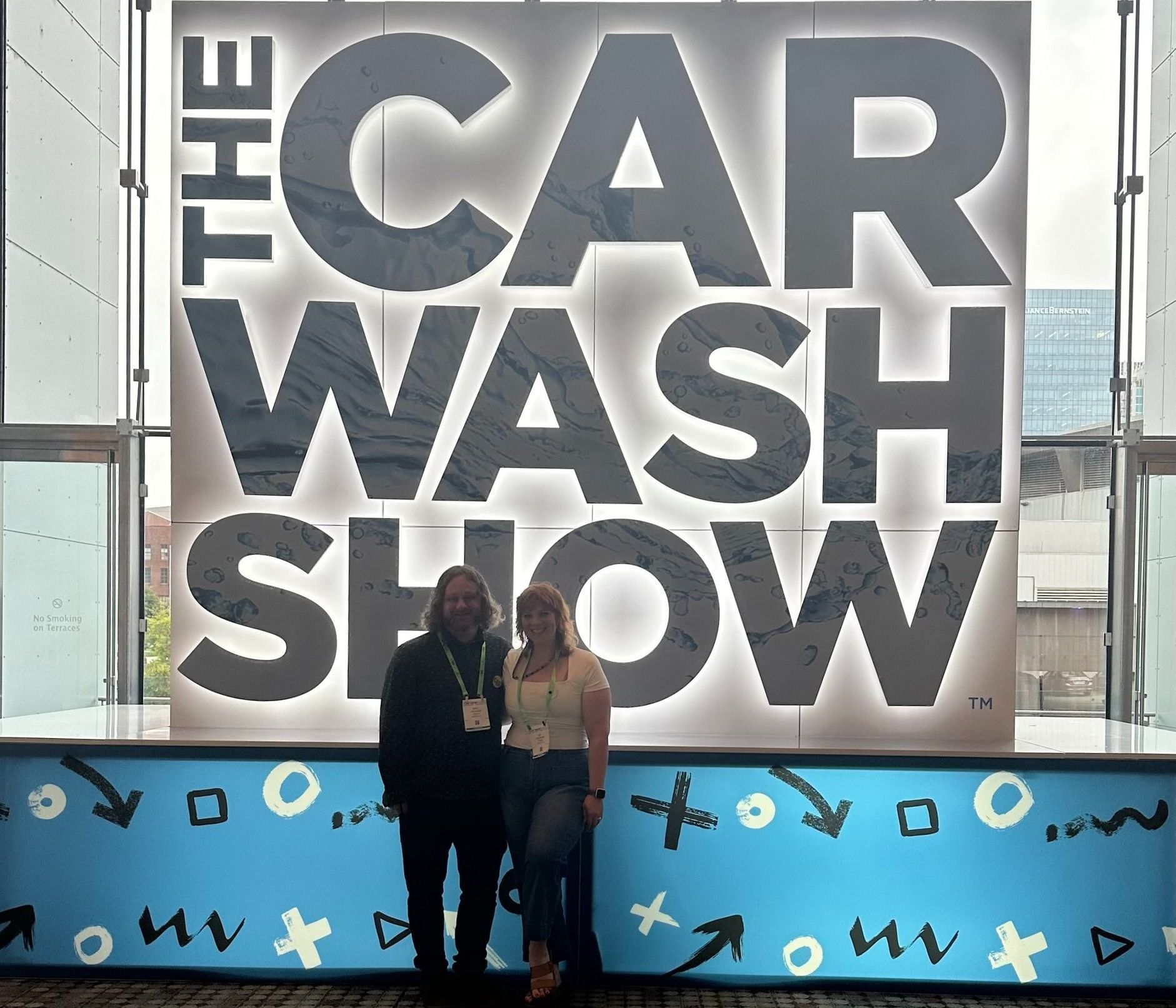 Mel & Mike standing in front of a sign that says the car wash show