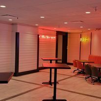 A room with tables and chairs in it and a neon sign on the wall