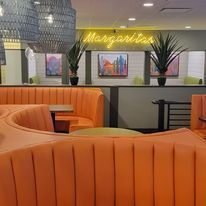 A restaurant with orange couches and a neon sign that says margaritas