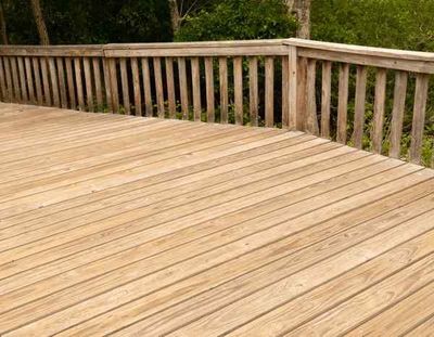 A preassure-treated wooden deck with a railing and trees in the background.