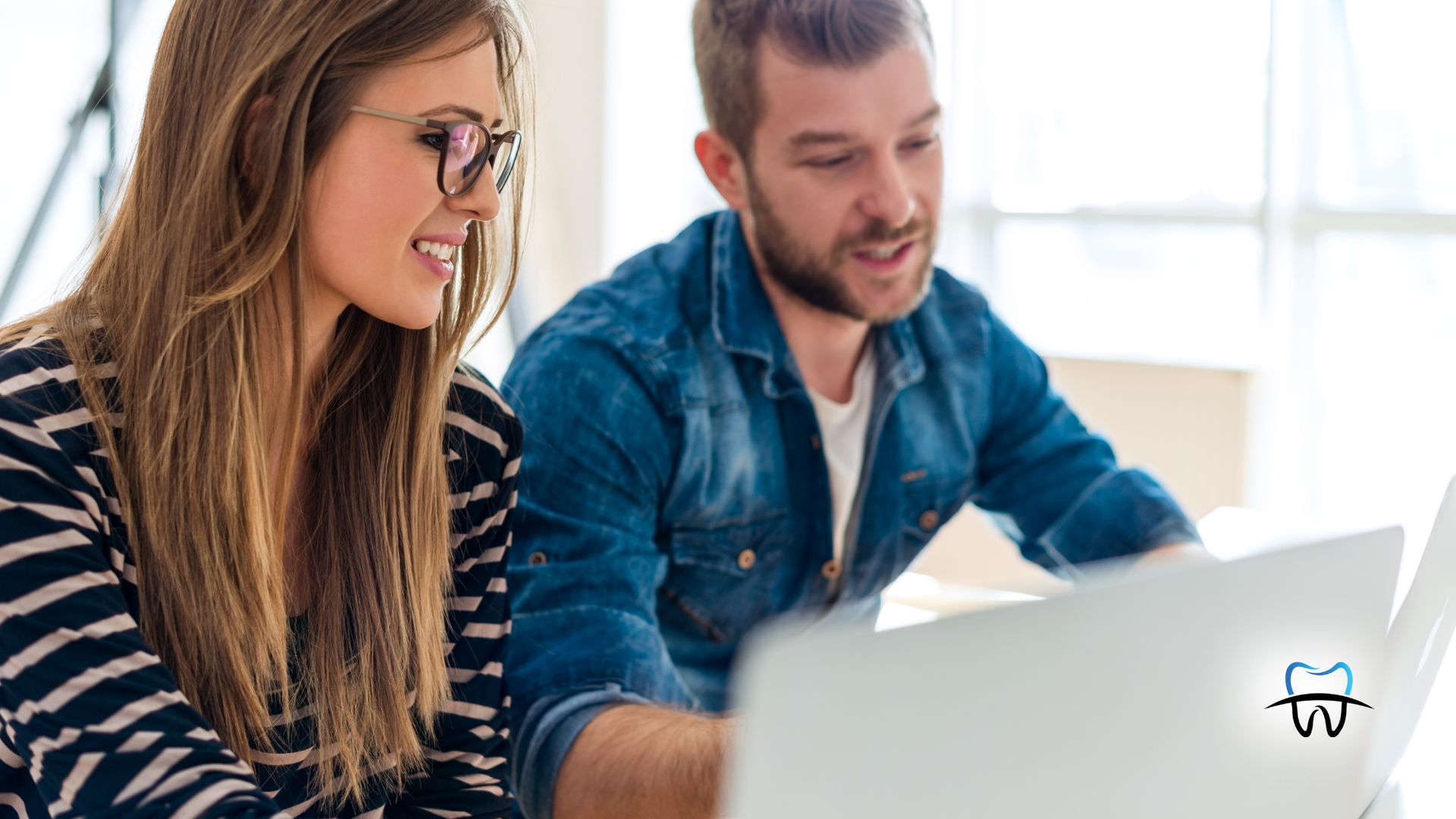 Woman with glasses and man in denim shirt looking at a laptop together, smiling.