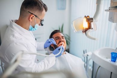 Dentist examining a patient's teeth with dental tools in a bright office setting.