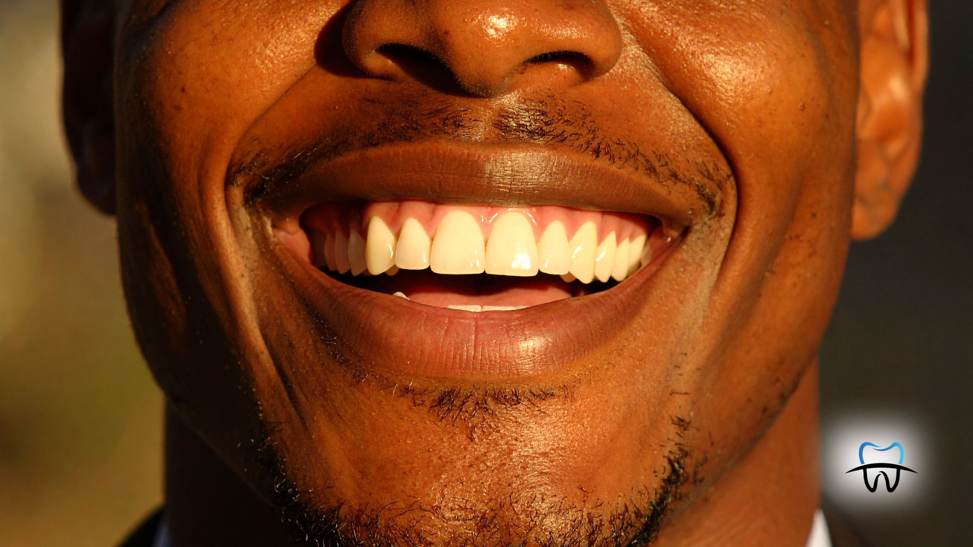 Close-up of a smiling person's mouth, showing white teeth against a brown complexion.