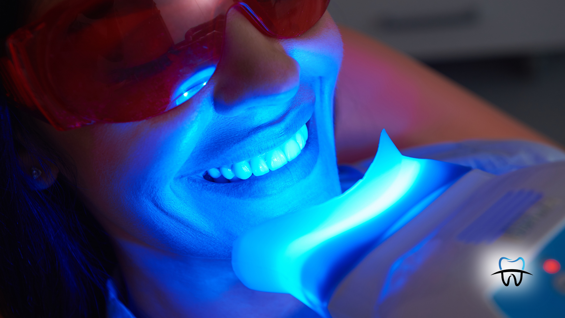 Person undergoing teeth whitening treatment with blue light, wearing protective glasses.