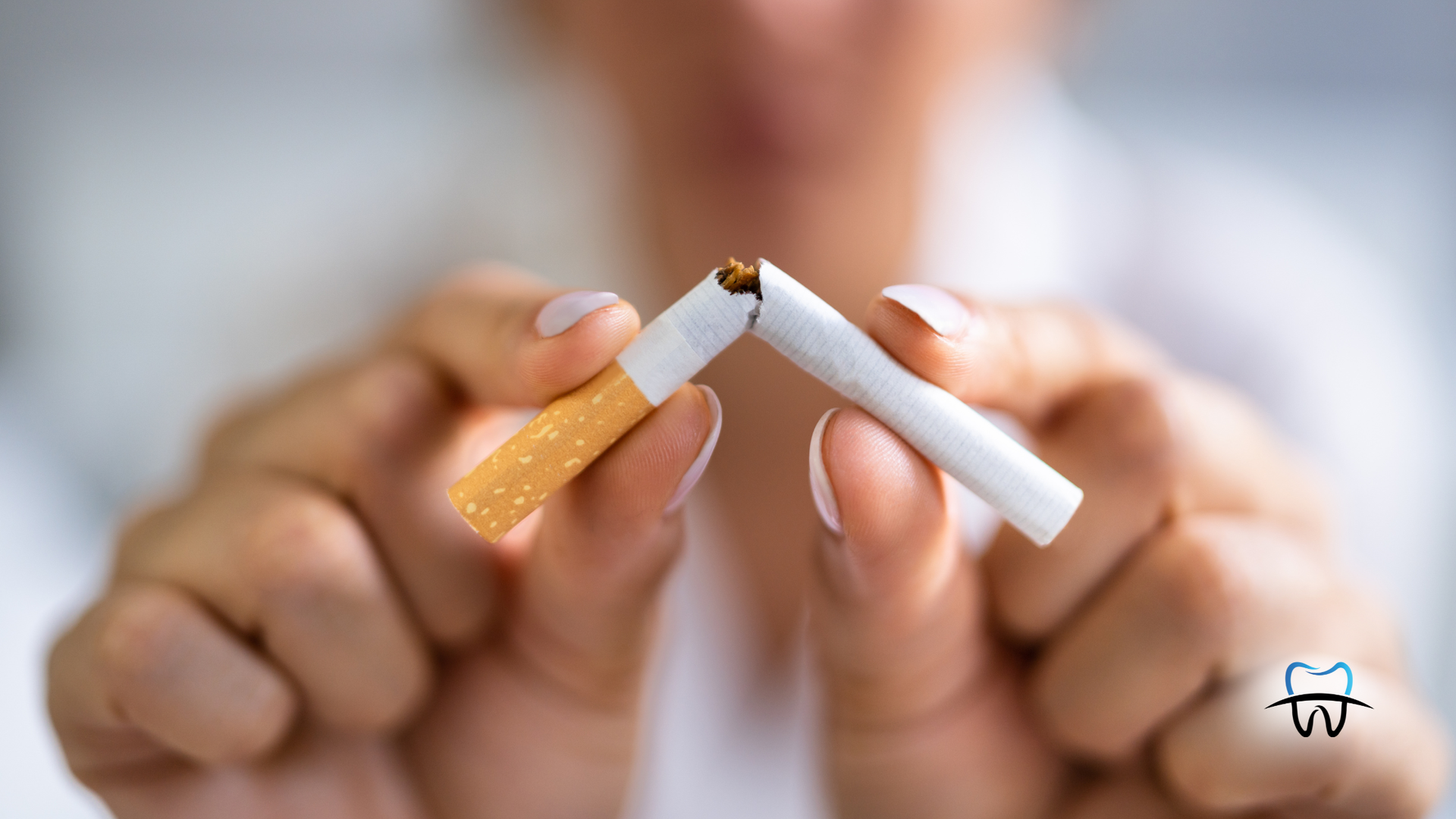 Person breaking a cigarette in half, white shirt, blurry background.