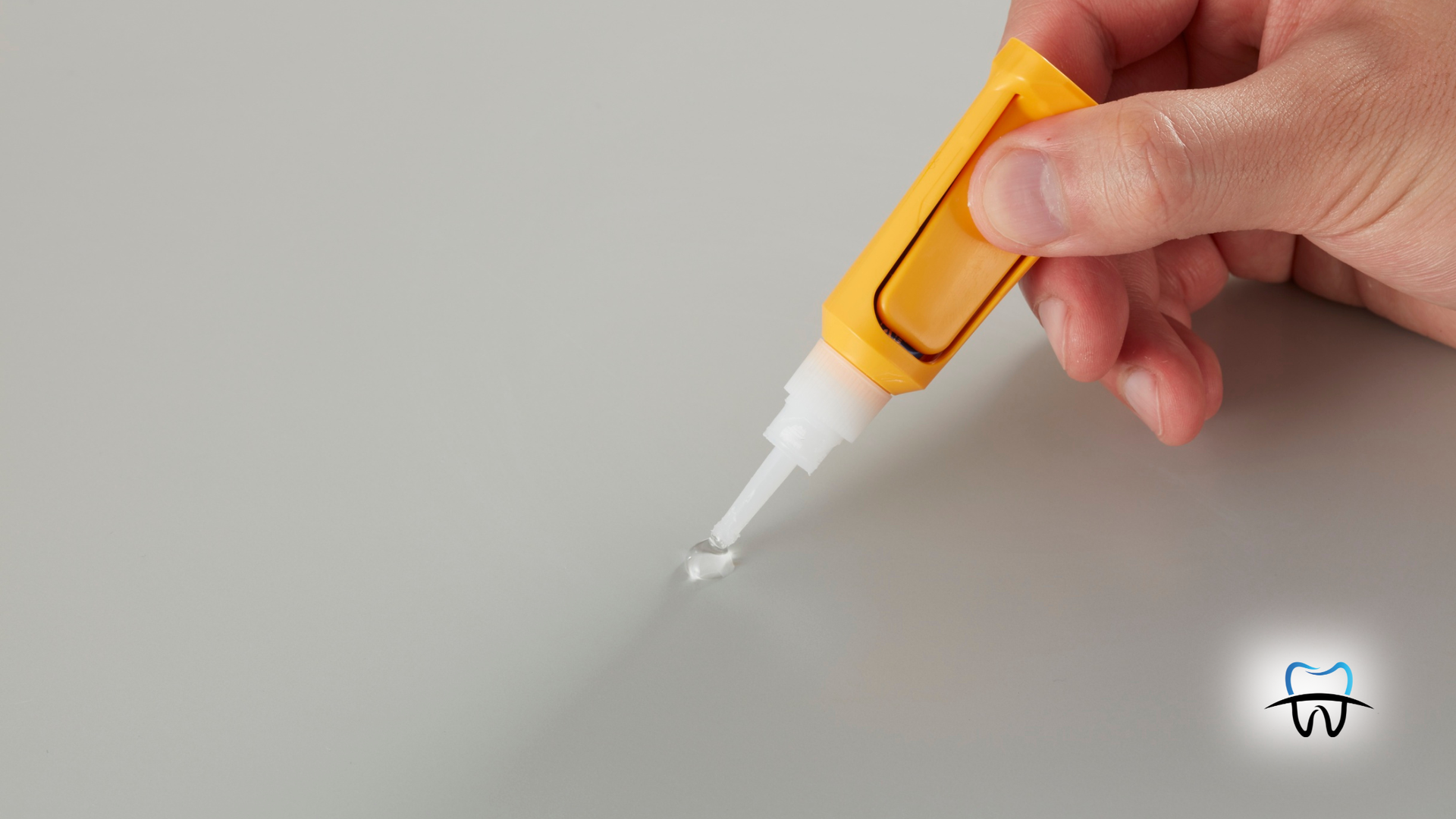 Hand applying glue from yellow bottle to a small spot on a gray surface.