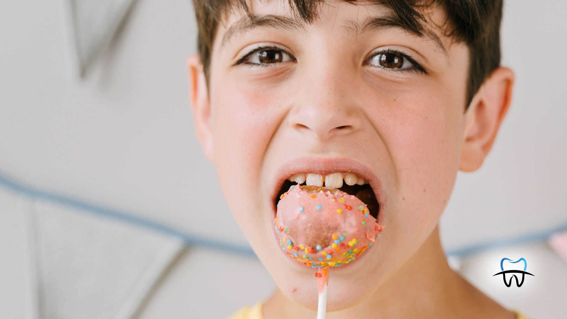 Boy opening mouth wide to eat a sprinkle-covered pink lollipop.