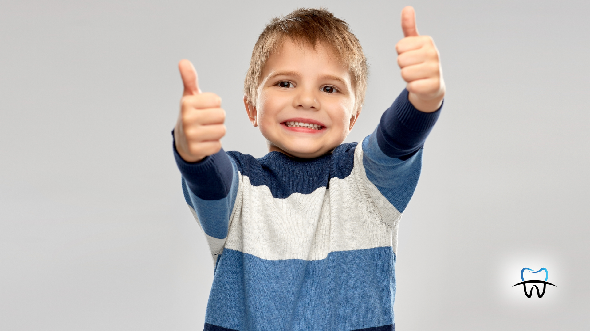 A smiling child with two thumbs up, wearing a blue and white striped sweater.