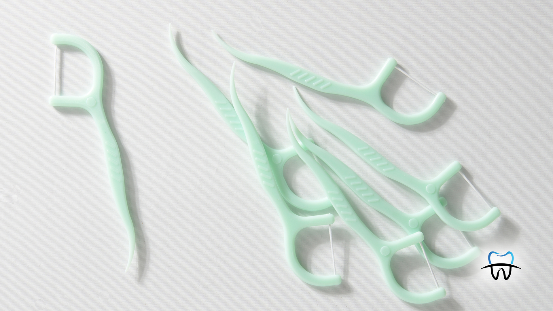 Several mint-green floss picks on a white surface, one isolated and others clustered.