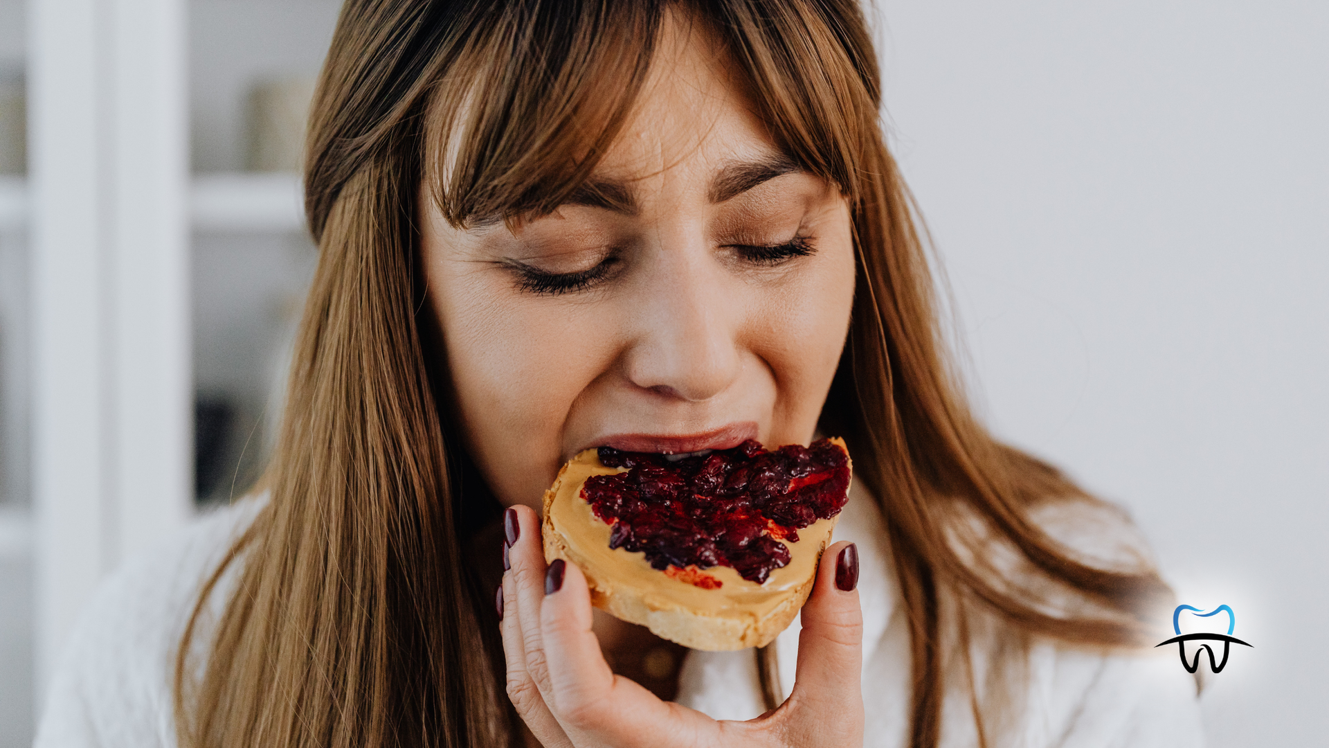 Woman eating a slice of bread topped with red jam.