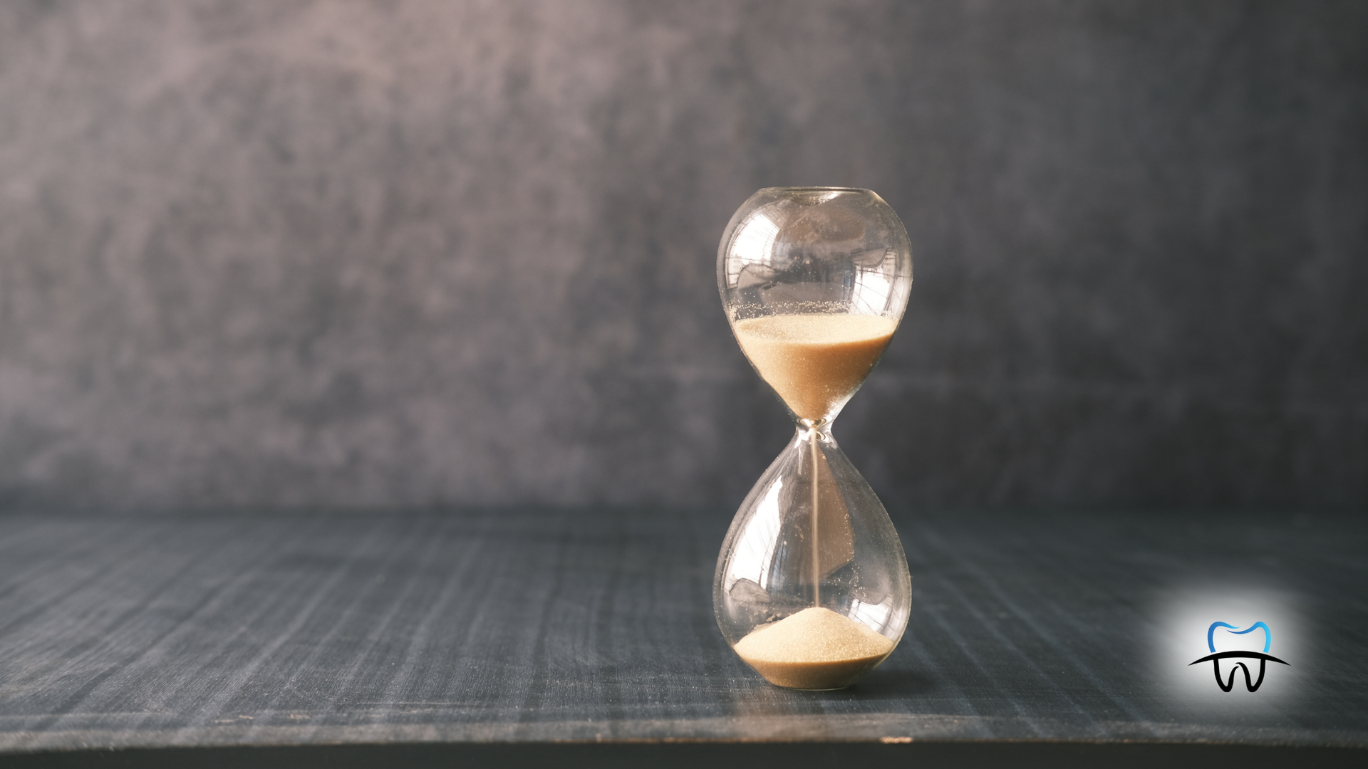 Hourglass on dark wood surface, sand flowing downwards.