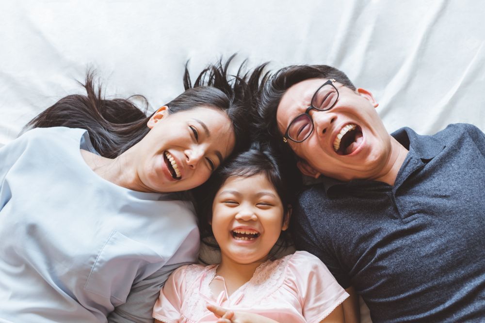 Family of three, smiling and laughing while lying on a white surface.