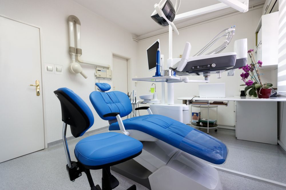 Blue dental chair in a bright, modern dental office with equipment and a desk.