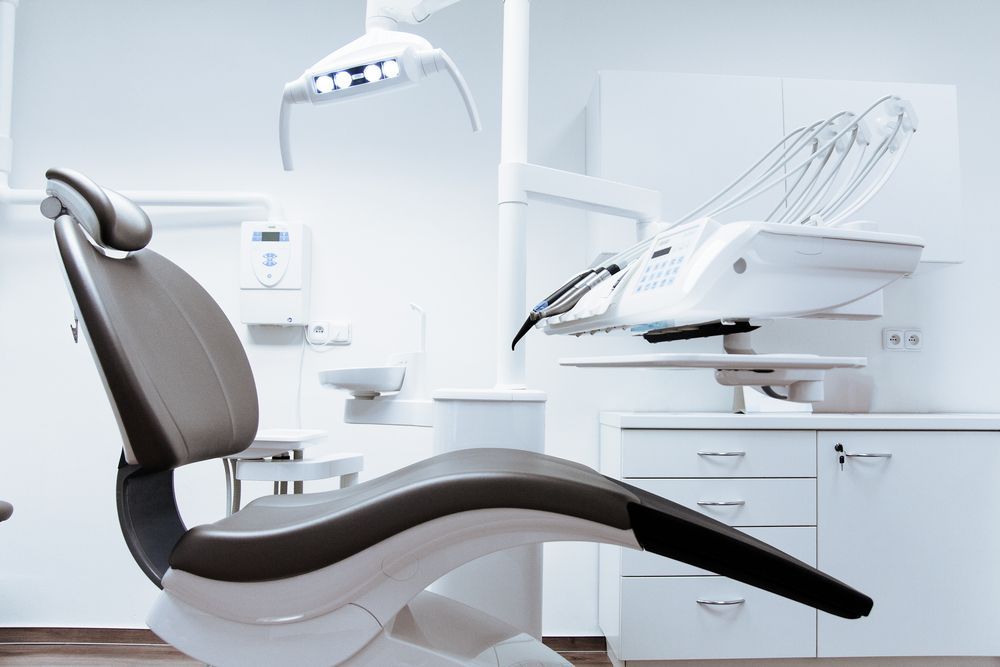 Dental chair with overhead light and equipment in a sterile white room.