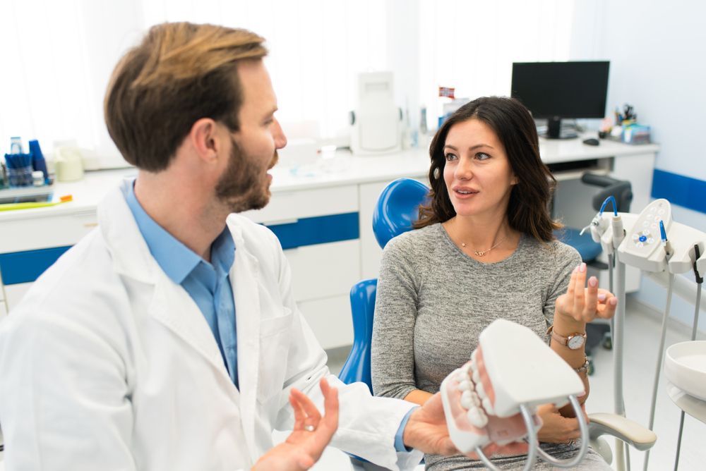 Dentist in white coat explains dental model to a patient in a dental office.