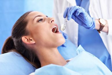 Woman at dentist's, mouth open, examined with mirror. Blue dental cloth, gloves.