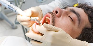 A person receiving dental work, mouth open. Dentist holds tool.