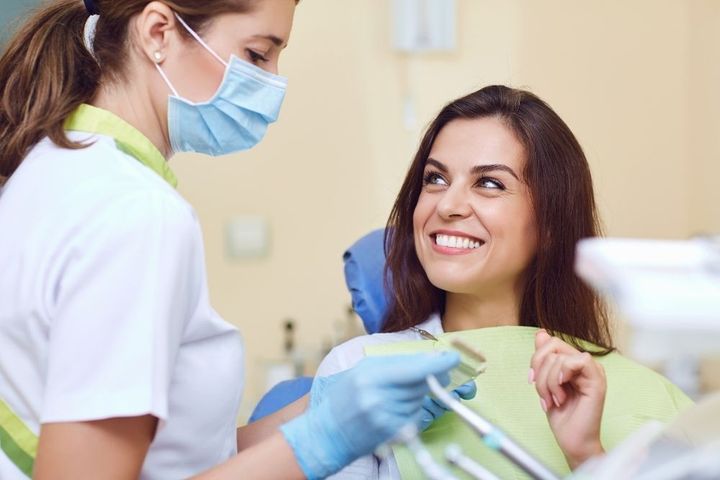 Dentist examining a patient's teeth. The patient smiles, wearing a green bib.