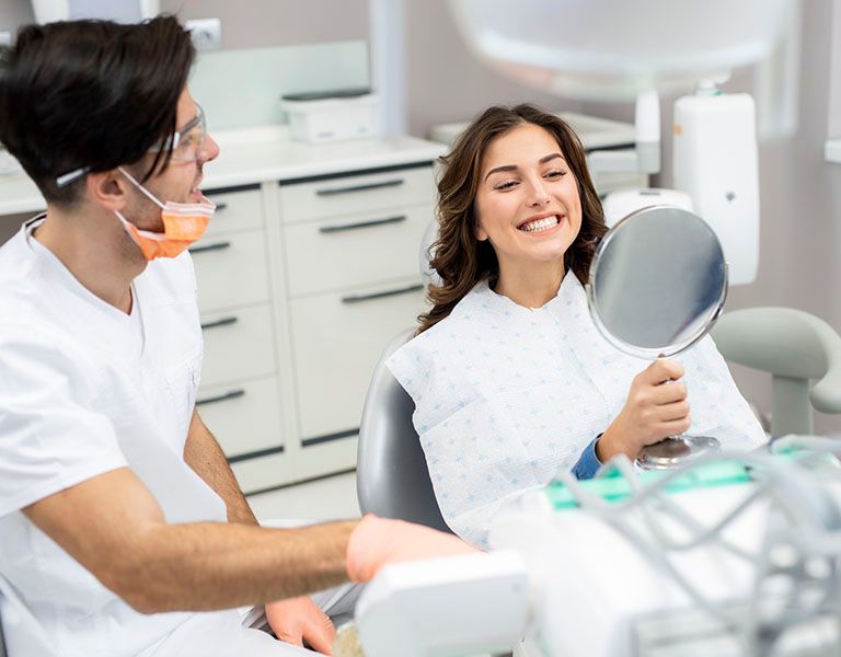 Dentist and patient in dental office. Patient smiles, looking at teeth with mirror.