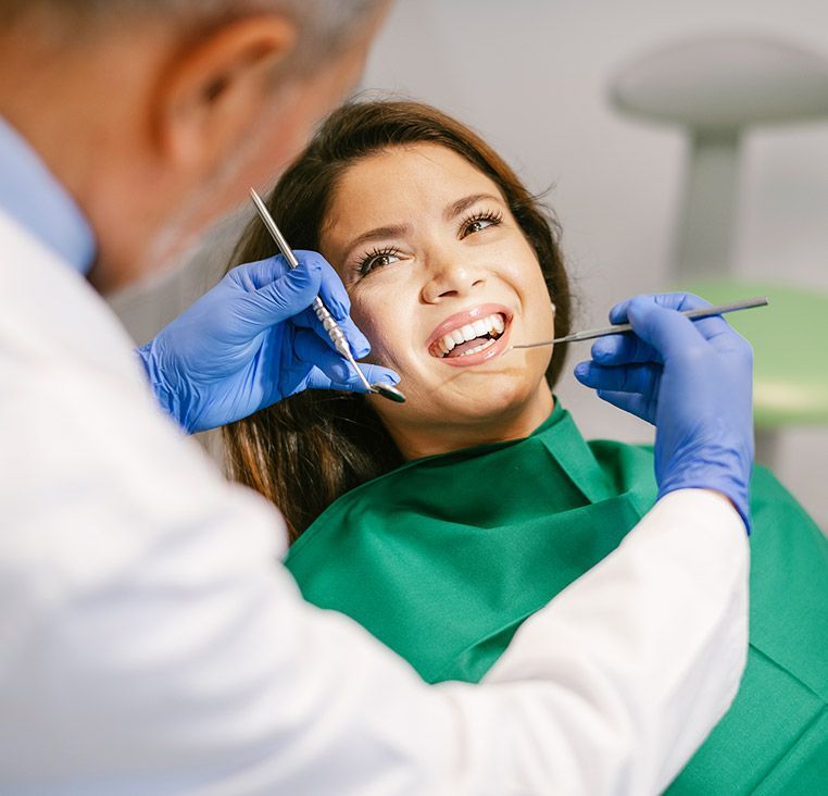 Dentist examining a patient's mouth; woman appears in pain.