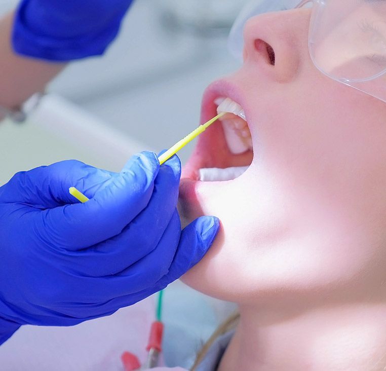 Dentist's gloved hand with tool inside a person's open mouth during a dental examination.