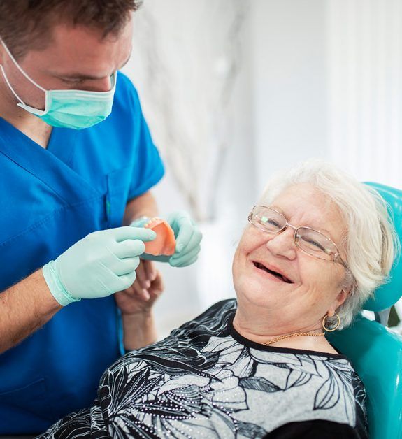 Dentist showing a dental model to a smiling patient in a dentist's chair.