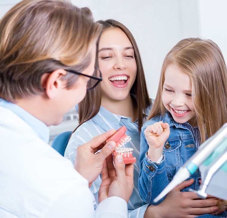 Dentist showing teeth model to a smiling child and parent in a dental office.