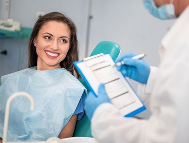 Woman in dental chair smiles at dentist with clipboard.