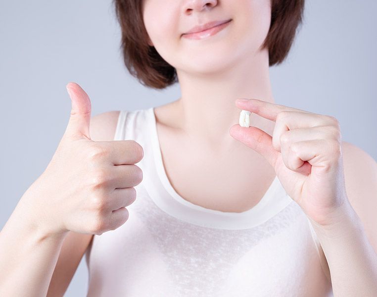 Woman holding a pill, smiling, and giving a thumbs-up.