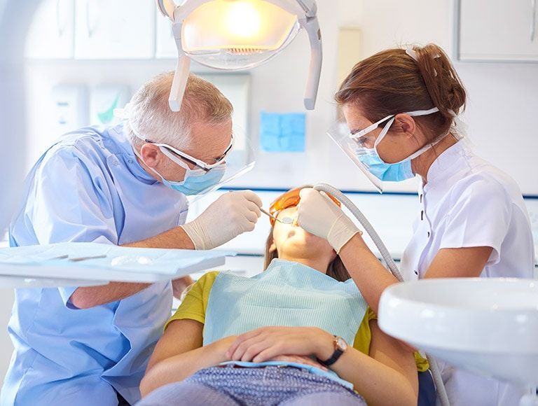 Dentist and assistant examining a patient's teeth under a bright light in a dental office.
